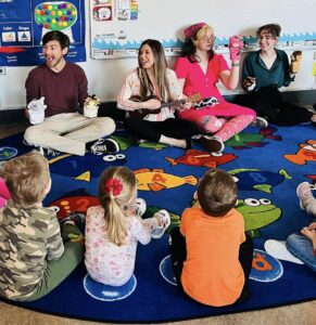 Dr. Cassandra Eisenreich playing the ukulele and her students holding up puppets to teach music to preschoolers 