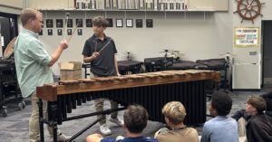 band director watches as student plays marimba