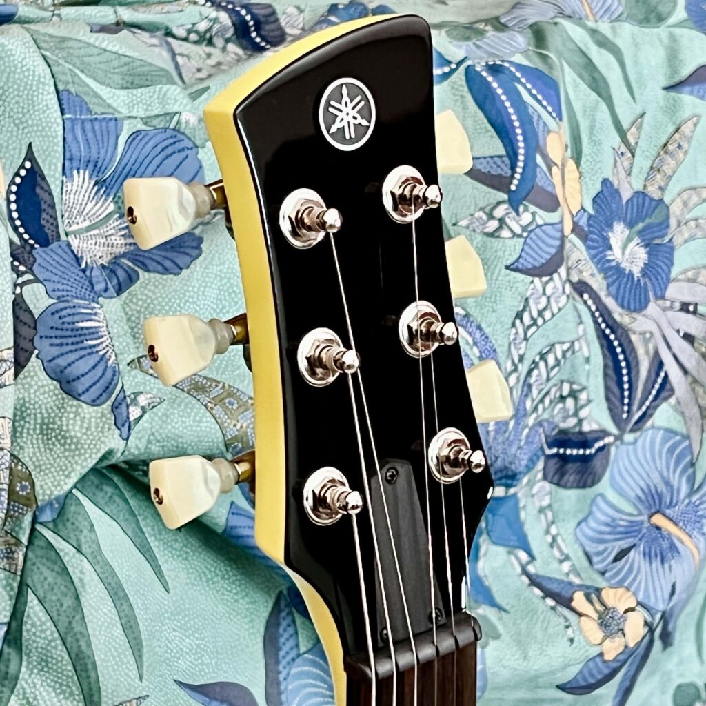 The black headstock of an electric guitar with ivory tuners.