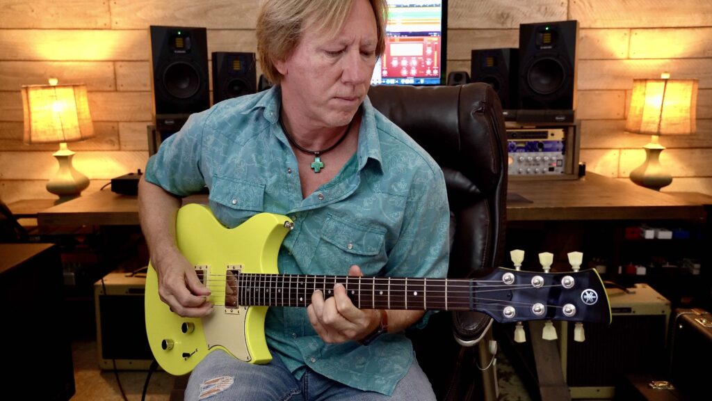 A man playing a yellow electric guitar in a home studio.