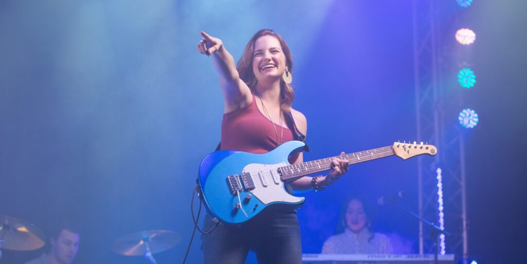 female guitarist on stage and pointing toward audience