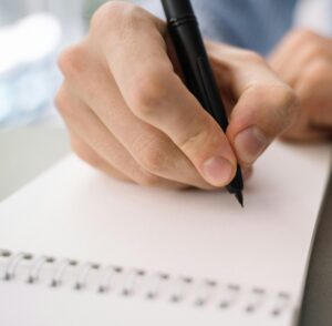 hand holding pen over notebook page, ready to write