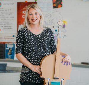 Annie Ray holding cardboard cello, which is used by her Crescendo Orchestra students