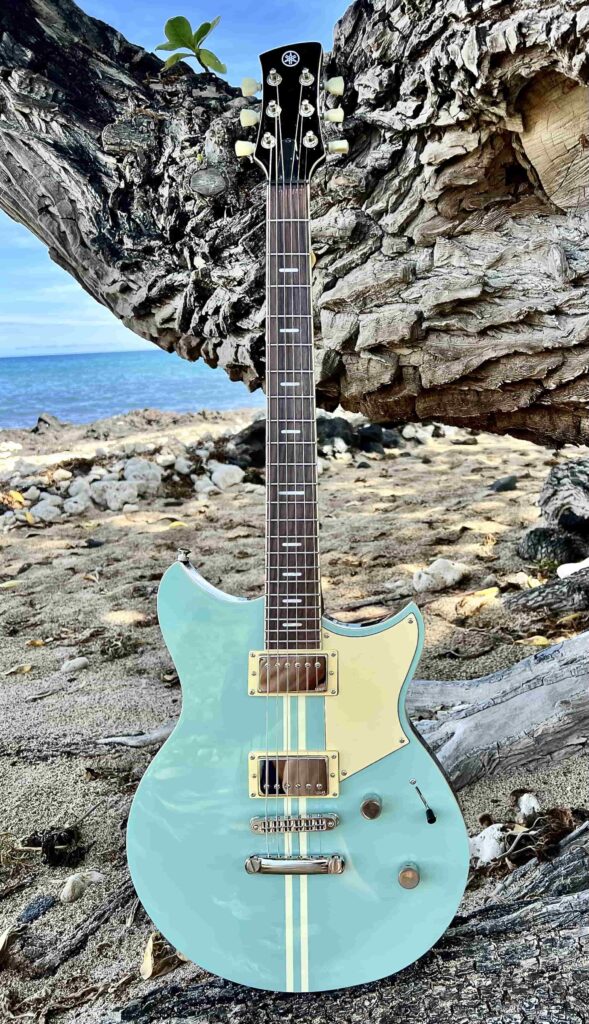 A blue-green electric guitar photographed on the beach.