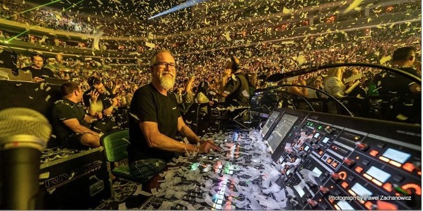 man smiling in front of an audio mixer with a crowd behind him