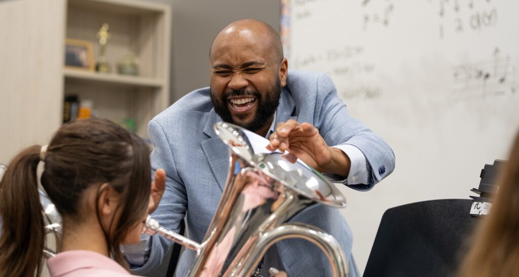 smiling music teacher helping student playing tuba