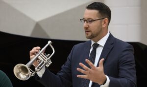 Dr. Aaron Witek lecturing while holding trumpet