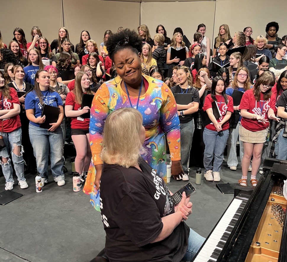 Coty Raven Morris speaking to pianist with choir behind her