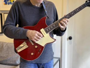 A standing guitarist holding an electric guitar with the strap relatively short.