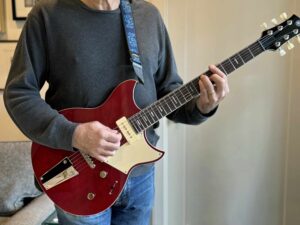 A standing guitarist holding an electric guitar with the strap at standard length.