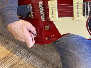 A hand turning the tone control on an electric guitar.