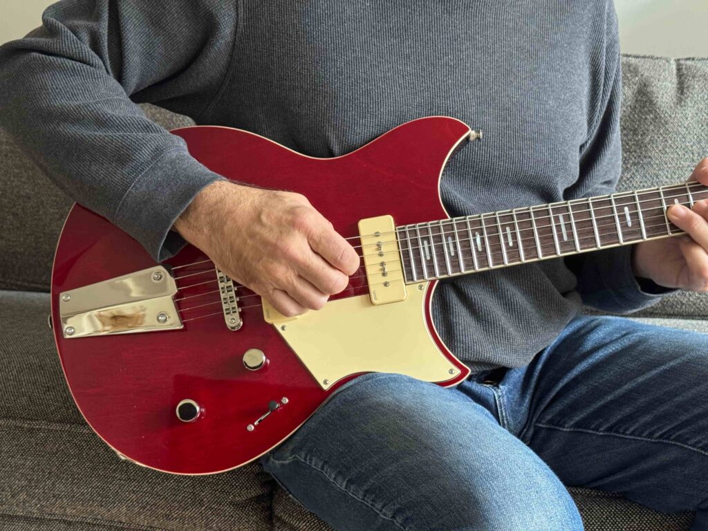 A seated guitarist holding an electric guitar.