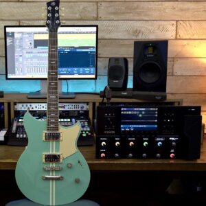 A green solid-body electric guitar next to an effects processor.