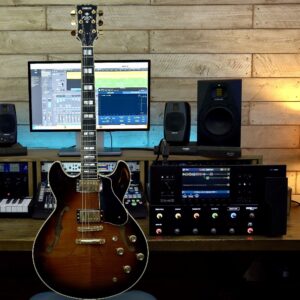 A sunburst semi-hollow-body electric guitar next to an effects processor.