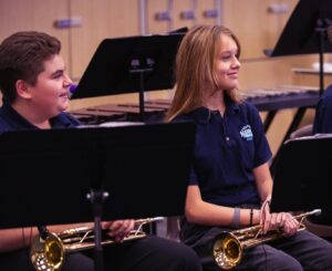 two students holding trumpets on lap during rehearsal