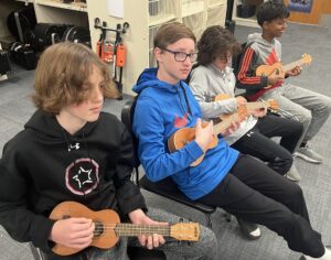 four students playing ukuleles 