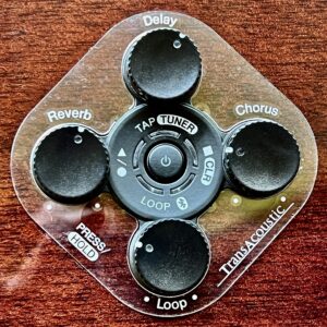 Closeup of a control panel on a guitar showing a round touchswitch surrounded by four knobs in a diamond configuration.