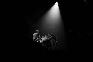 A man in the spotlight playing a piano onstage.