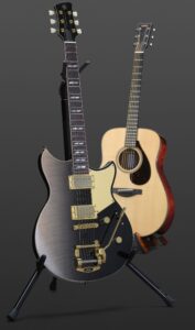 An electric guitar and an acoustic guitar, both on stands.