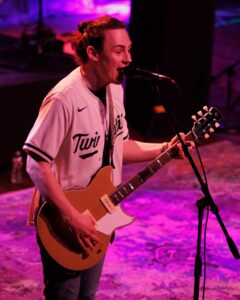 A man playing an electric guitar while singing into a microphone.