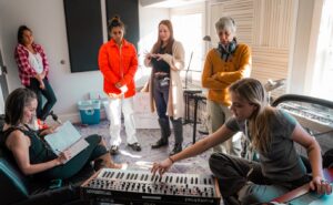 six women talking and taking notes around a synthesizer