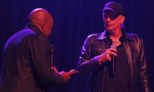 Nathan East and Billy Sheehan holding microphones at a concert.