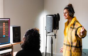 on woman standing in front of mic while another woman is sitting at computer