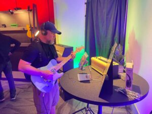 A man playing guitar in front of a table at a trade show.