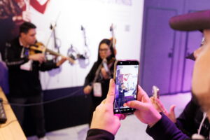 Someone using their phone to capture an imate of two violinists performing at a trade show.