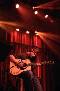 A man playing an acoustic guitar onstage.