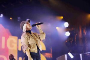 A blonde woman wearing a baseball cap singing into a microphone onstage.