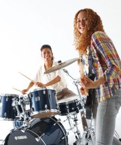 two girls -- one playing the drum set and the other on guitar 