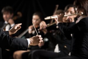 Conductor directing symphony orchestra with performers on background.