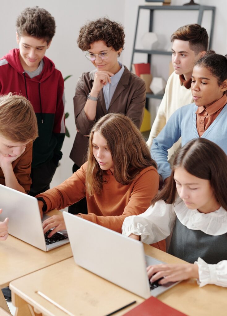 teacher and class gather around two students working on laptops