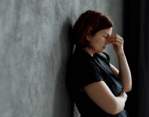 someone looking overwhelmed and leaning against a wall with their hand on their face
